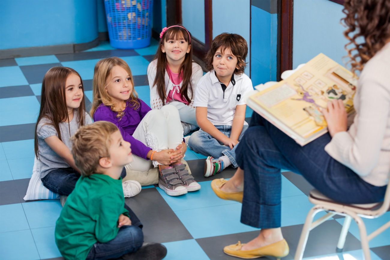 Teacher reading story book to children in kindergarten